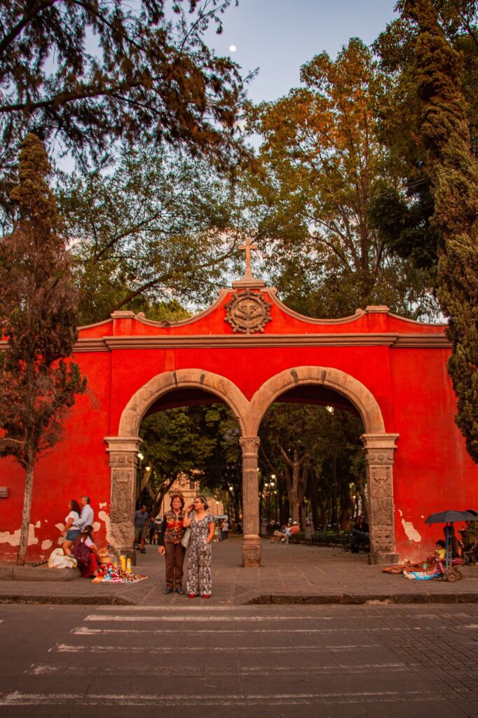 Imagen ilustrativa: acceso peatonal con arco y visitantes en un espacio público; no identifica la sede del evento.